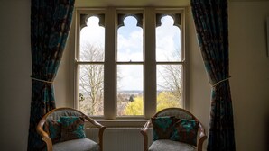 A room with two wooden chairs, a radiator, and a window with curtains. - Farnley Tower Guesthouse (Durham)