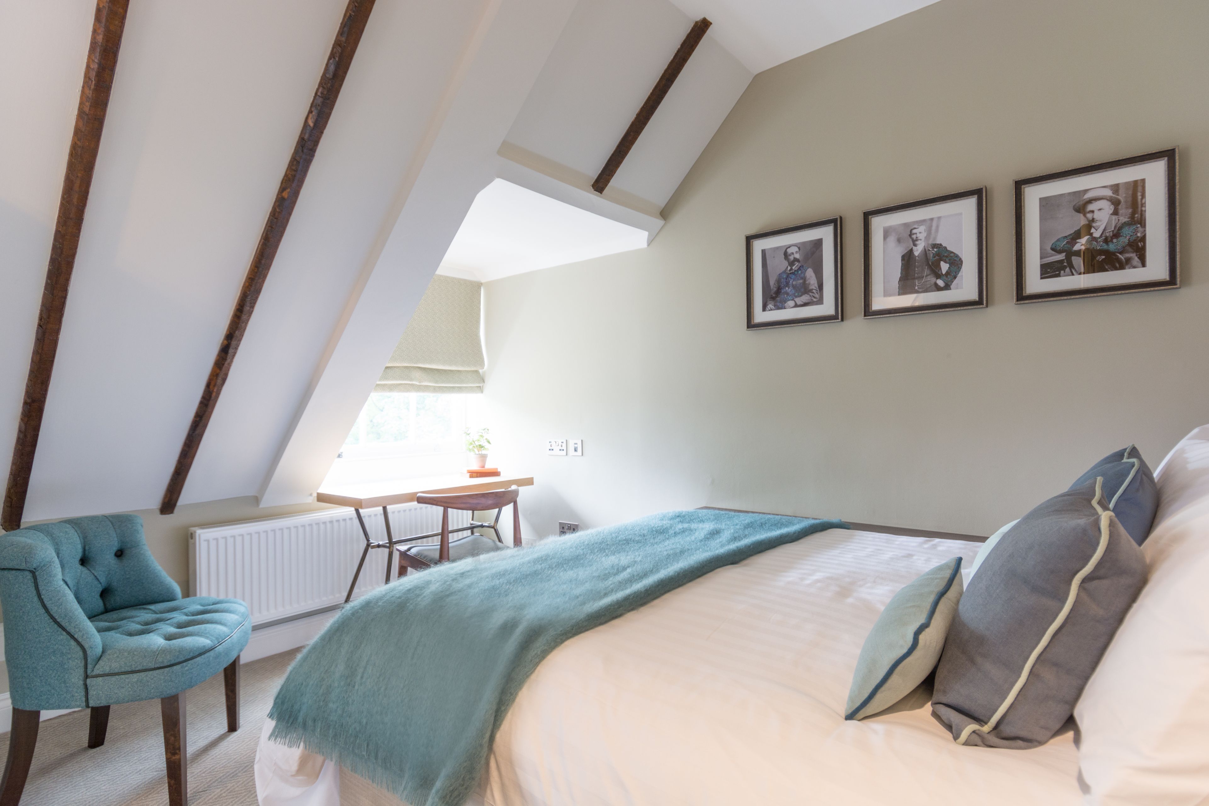 A bedroom with a sloped ceiling, a bed with pillows, a chair, and framed pictures on the wall.