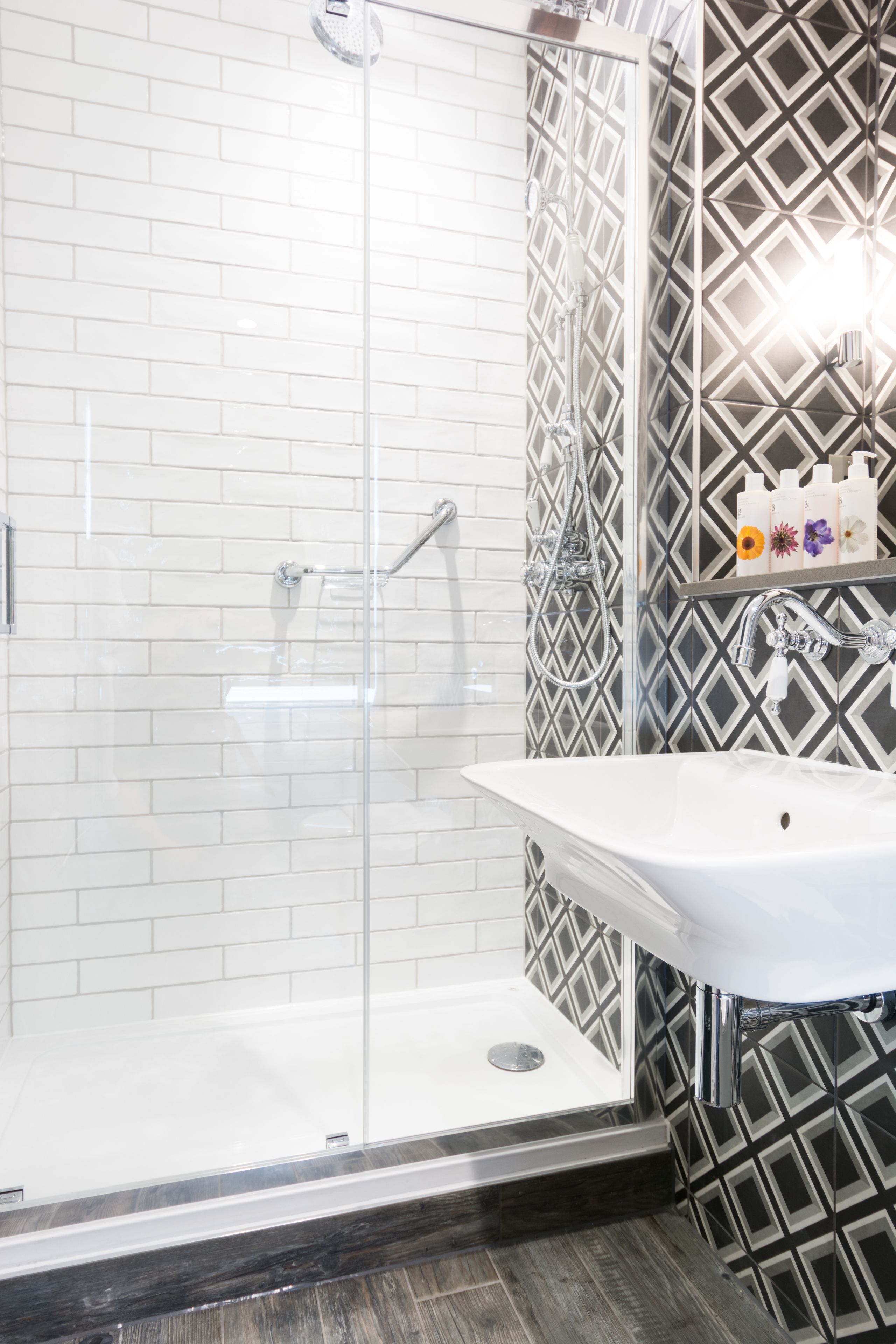 Un baño moderno con ducha envuelta en vidrio, un lavabo blanco y baldosas estampadas.
