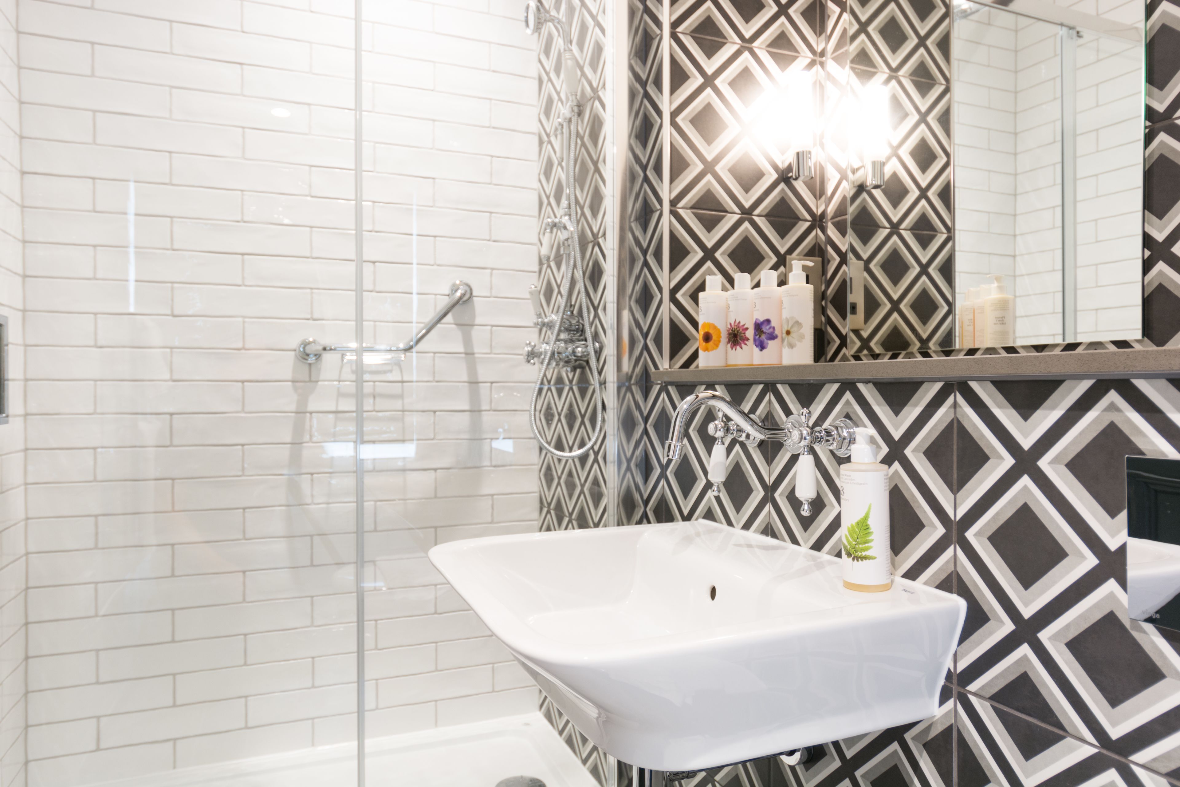 Un baño con lavamanos blanco, ducha y espejo.