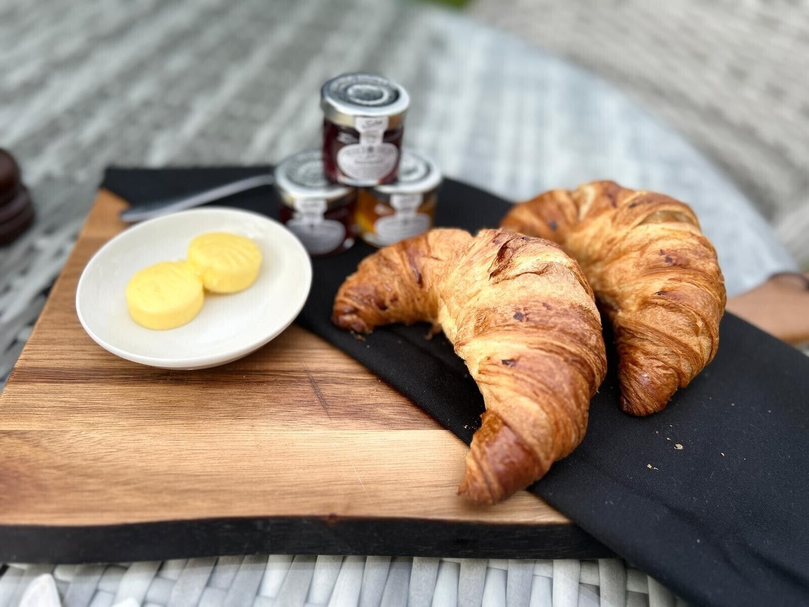 A wooden table with two croissants and a small plate of butter.