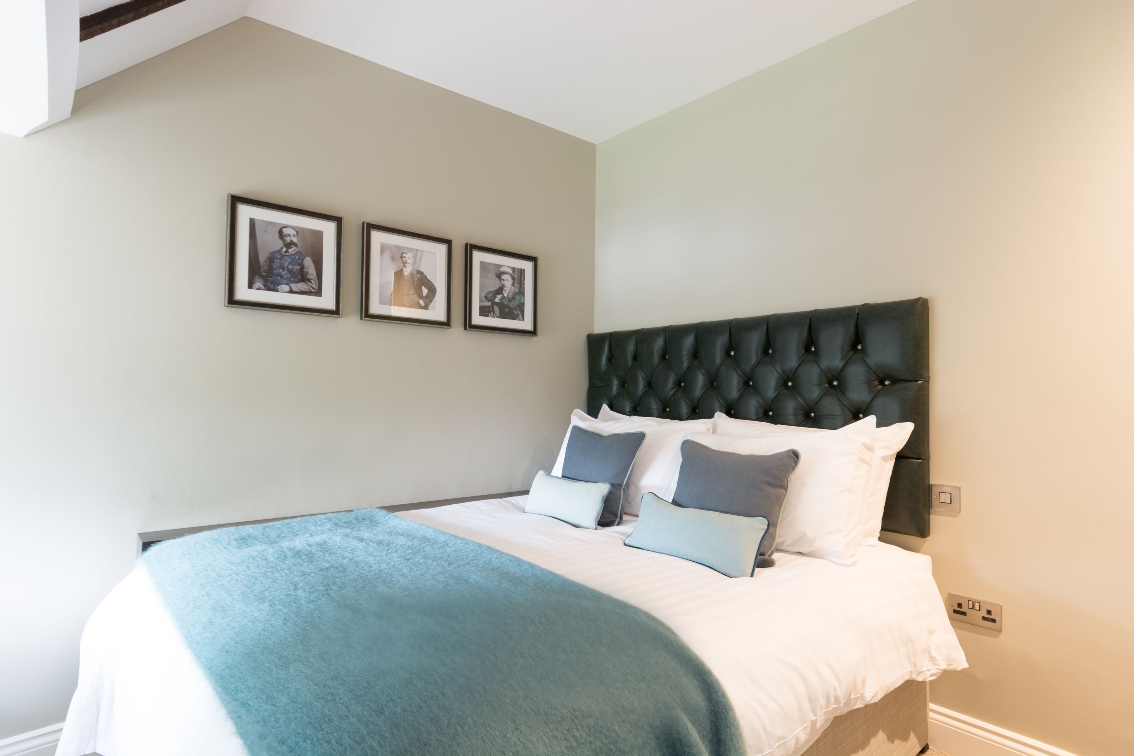 Une chambre à coucher avec un grand lit, une tête de lit capitonnée et trois tableaux encadrés accrochés au mur.