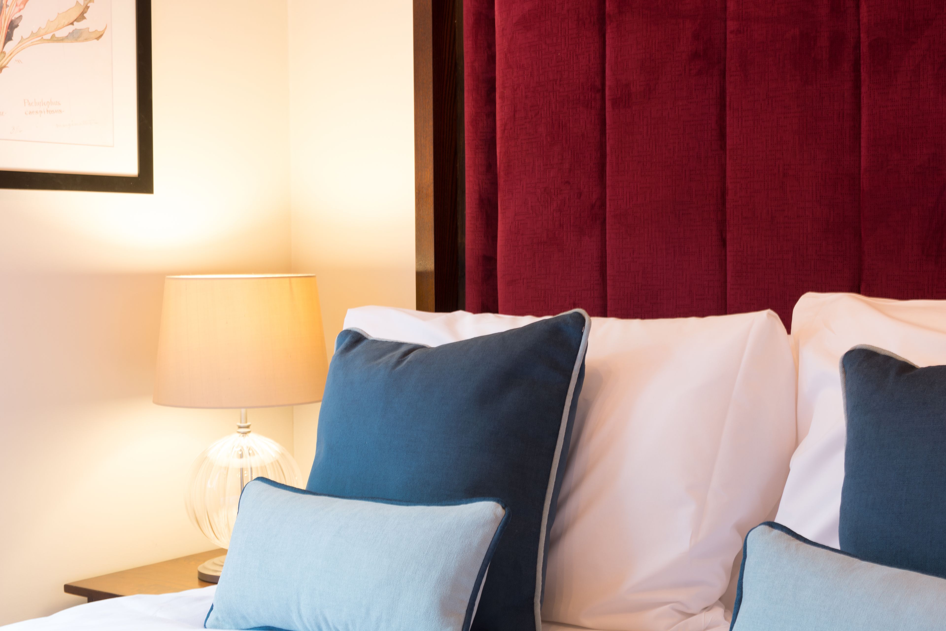 A hotel room with a bed, pillows, a lamp, and a red curtain.