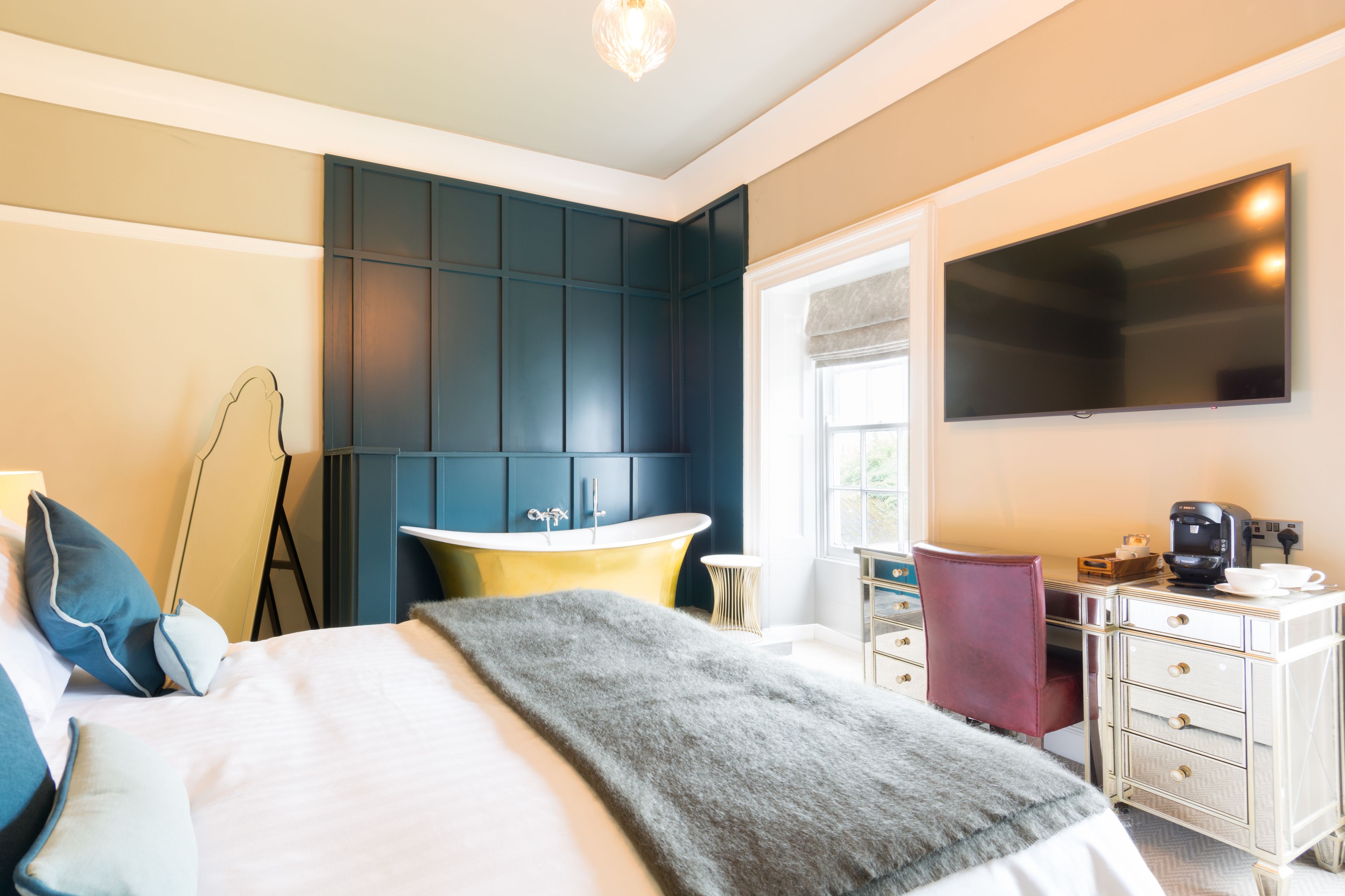 A hotel room with a bed, a desk, a chair, a flat-screen TV, a bathroom with a bathtub, and a window.
