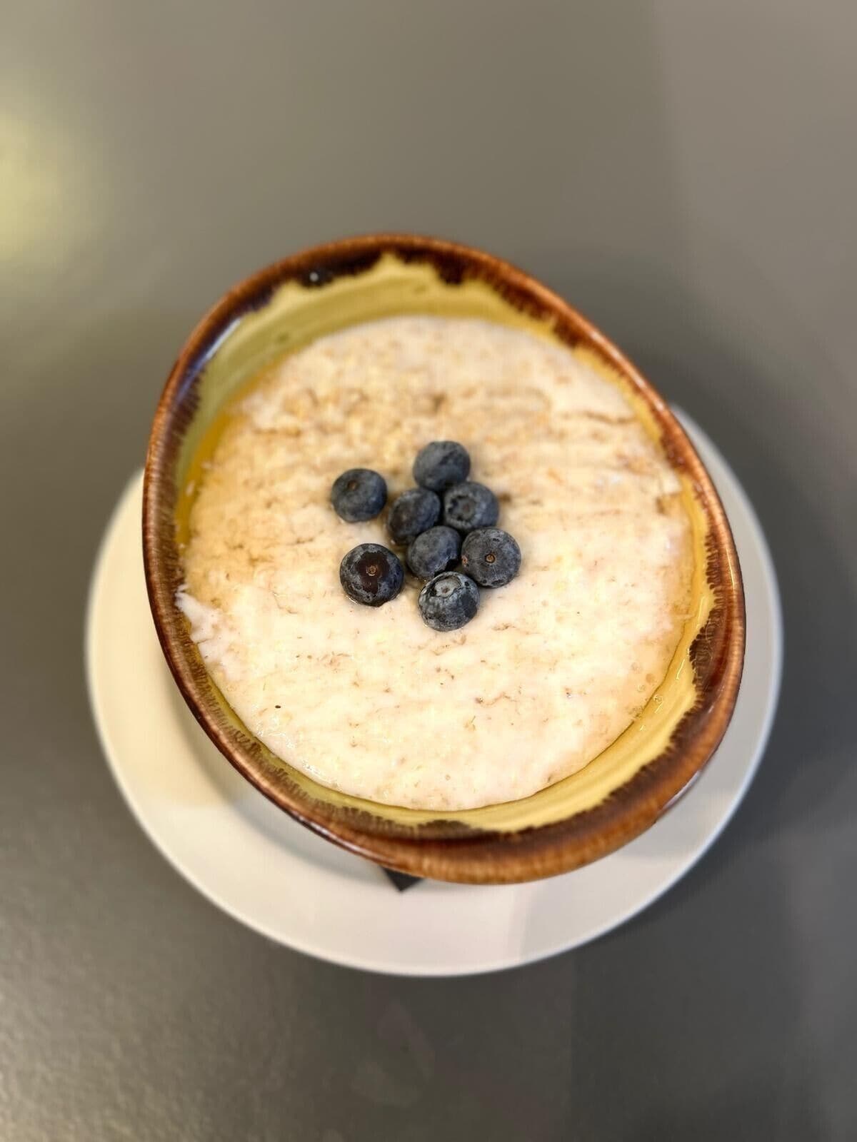 A bowl of oatmeal topped with blueberries on a white plate.