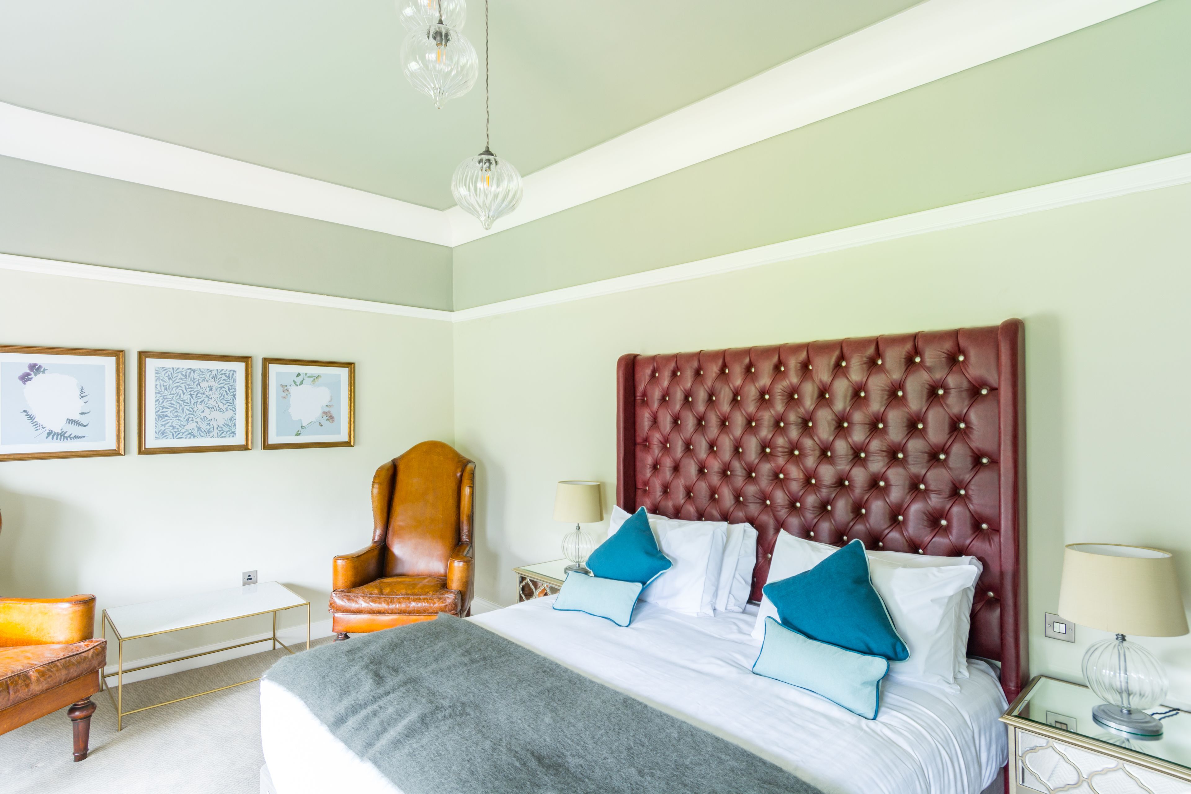 Un dormitorio ordenado con una cama grande, un sillón de cuero, una mesita y cuadros enmarcados en la pared.