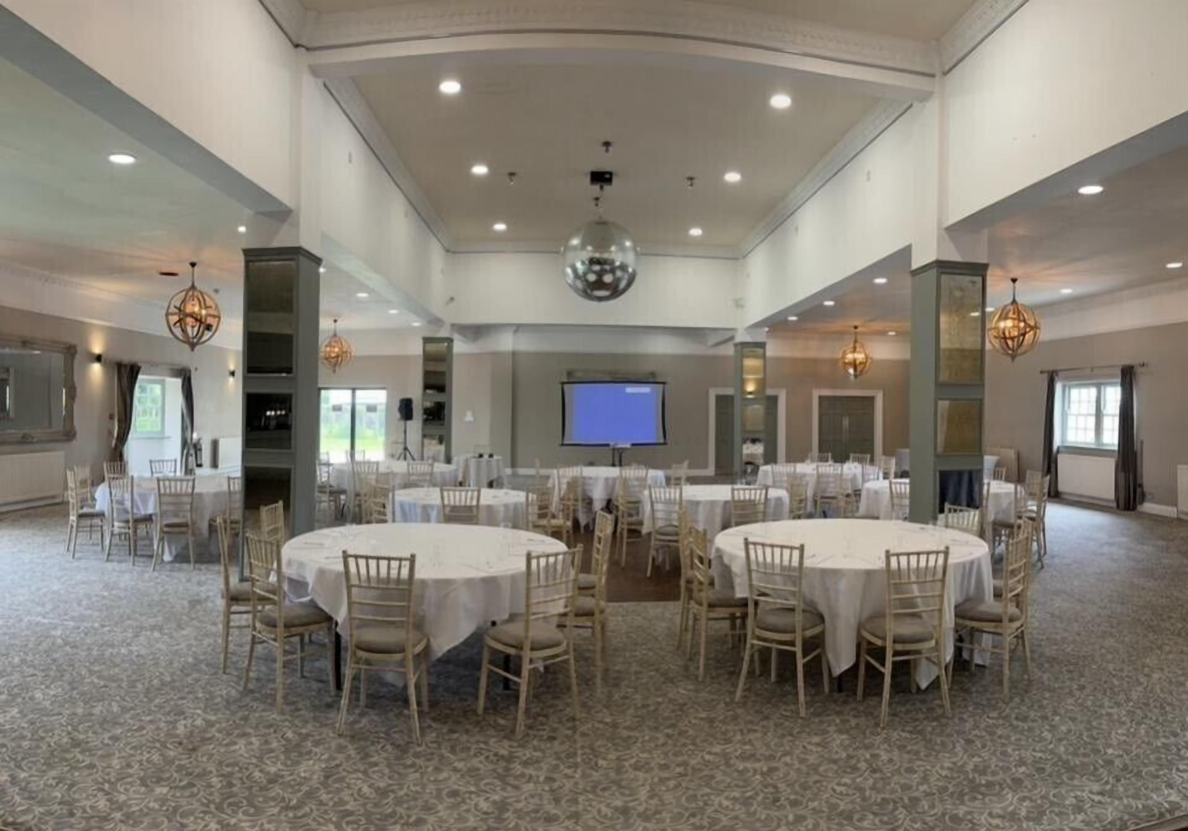Un salón de conferencias amplio con mesas y sillas redondas, una pantalla de proyector e iluminación decorativa.