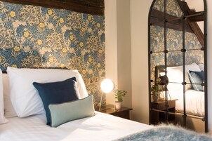Ein Schlafzimmer mit strukturierter Tapete, einem Bett mit weißer und blauer Bettwäsche, einem Nachttisch mit Lampe und einem Beistelltisch mit Pflanze.