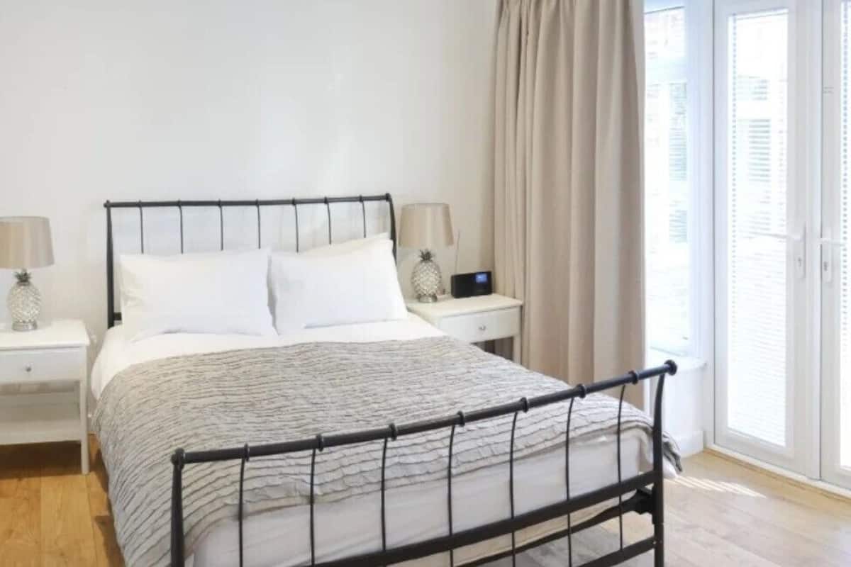 Un dormitorio con cama, mesitas de noche, una ventana con cortinas y vistas al exterior.