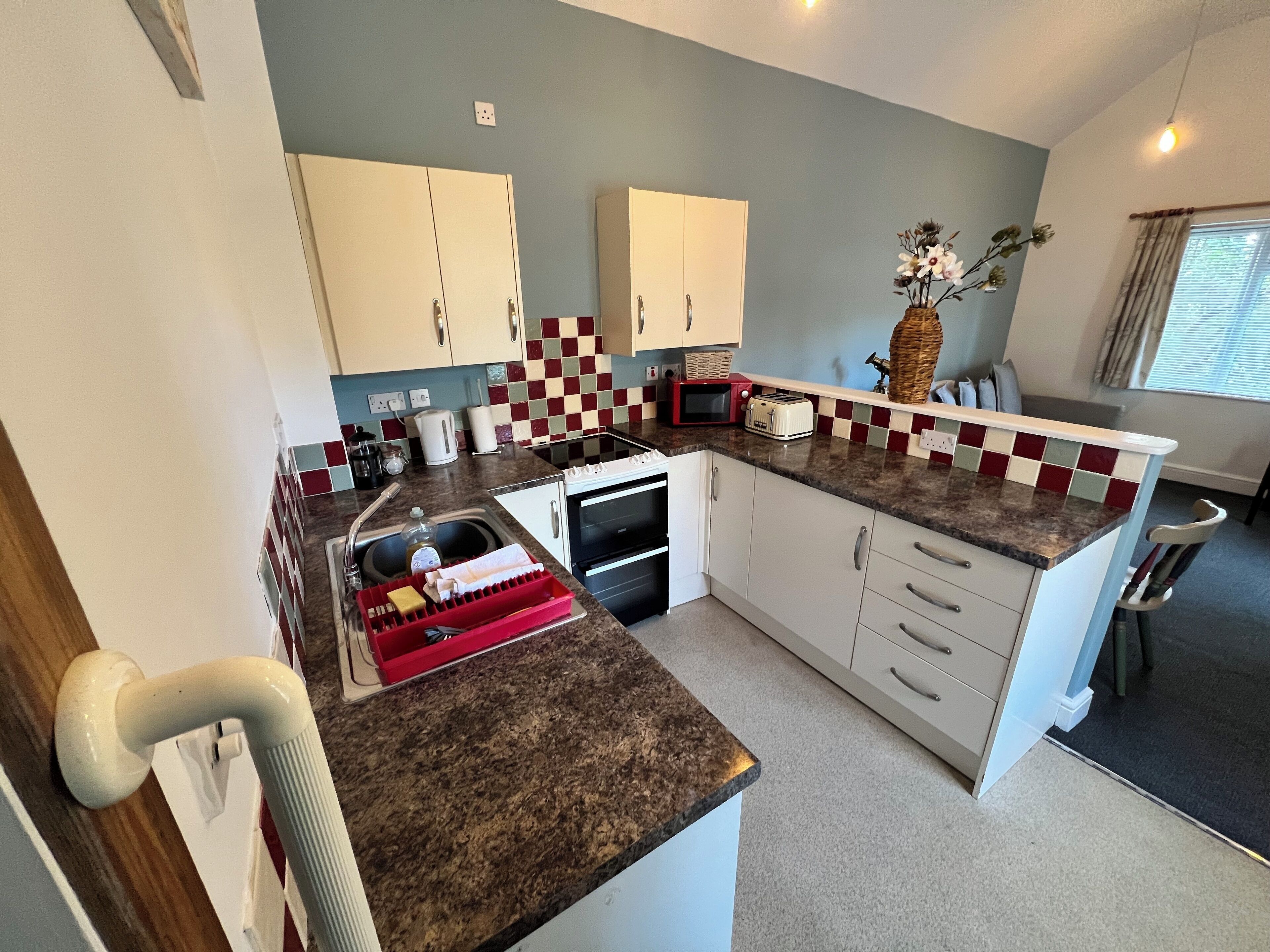 A compact kitchen with white cabinets, a granite countertop, a microwave, a toaster, and a sink.
