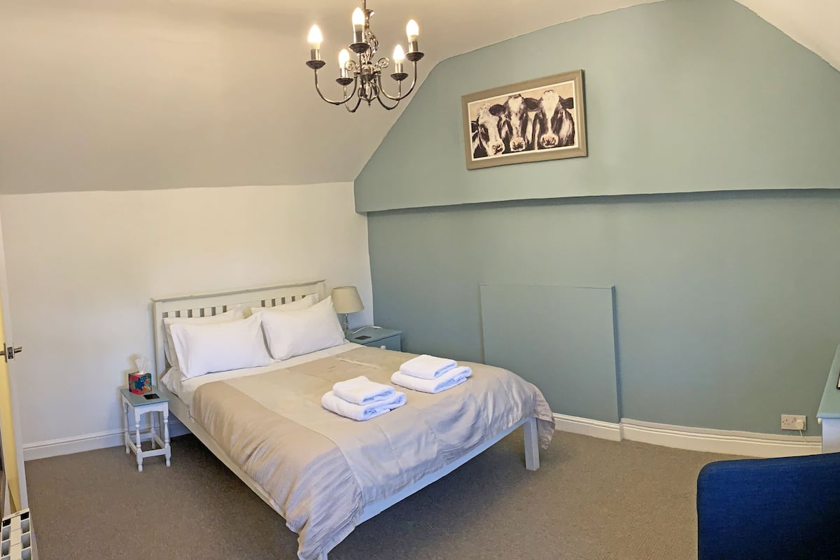 Un dormitorio con cama, mesita de noche, lámpara y televisión en la pared.