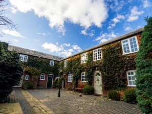 A courtyard with brick buildings, a paved walkway, and a bench. - Glendower House Apartments (Dereham)