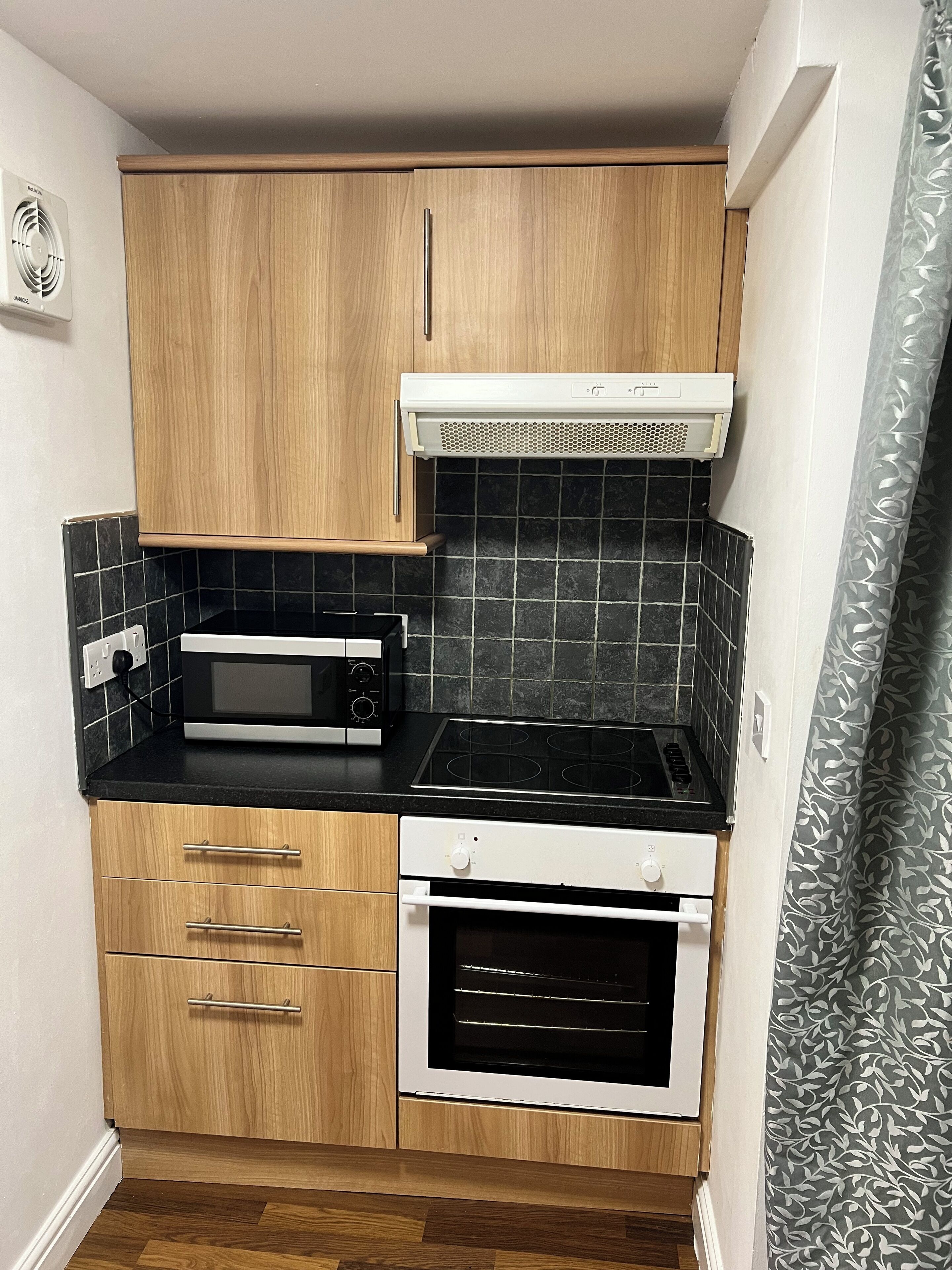 A compact kitchen with wooden cabinets, a microwave, a stove, and a built-in oven.