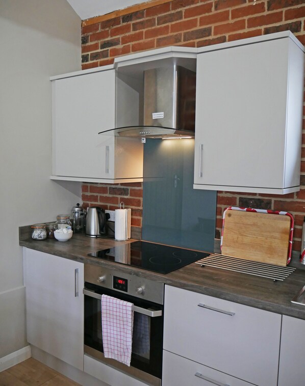 Una cocina compacta con armarios blancos, una campana extractora de acero inoxidable, un horno empotrado y una pared de ladrillo.