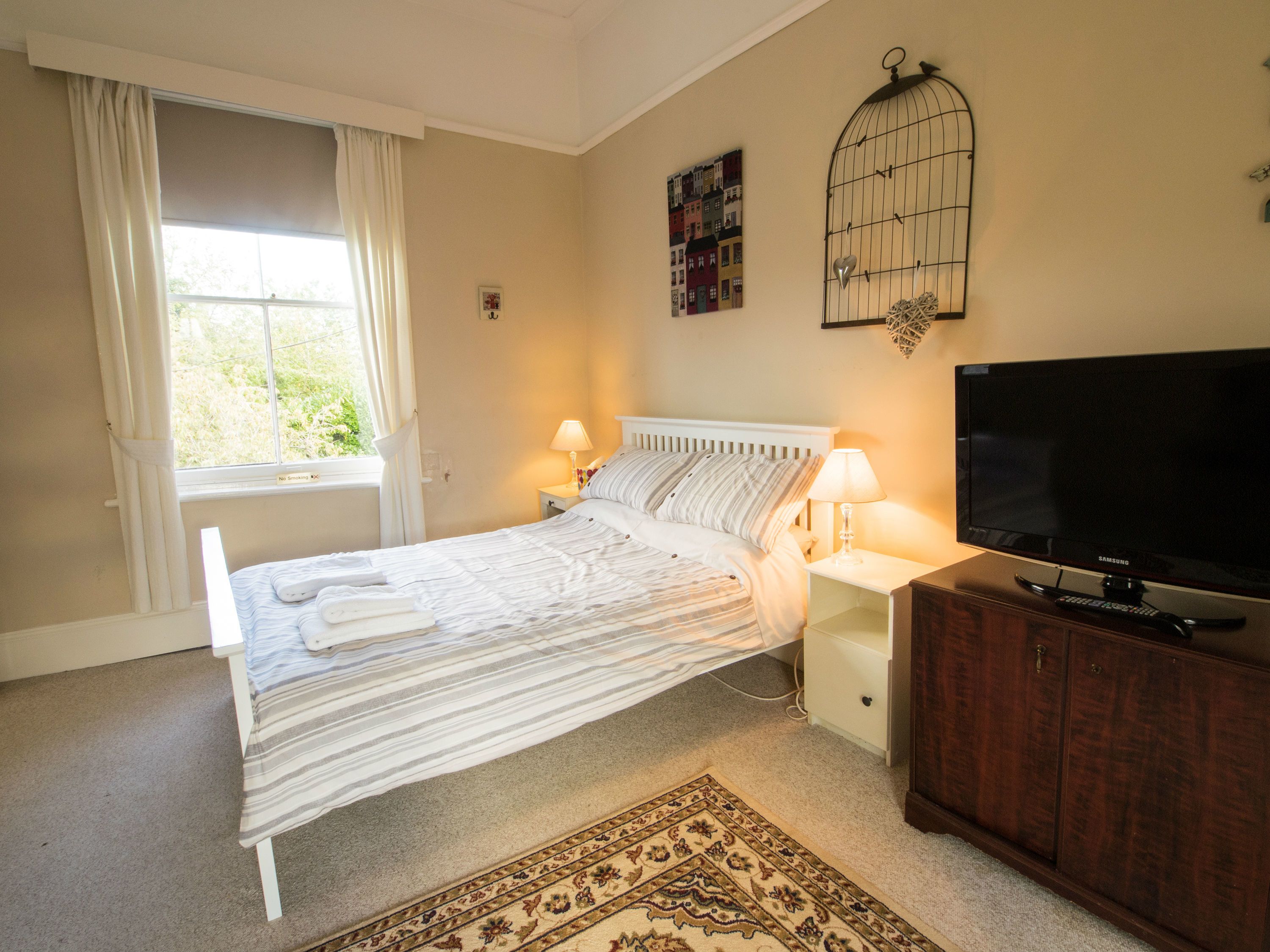 A bedroom with a bed, bedside lamps, a TV, a wooden cabinet, and a window with curtains.