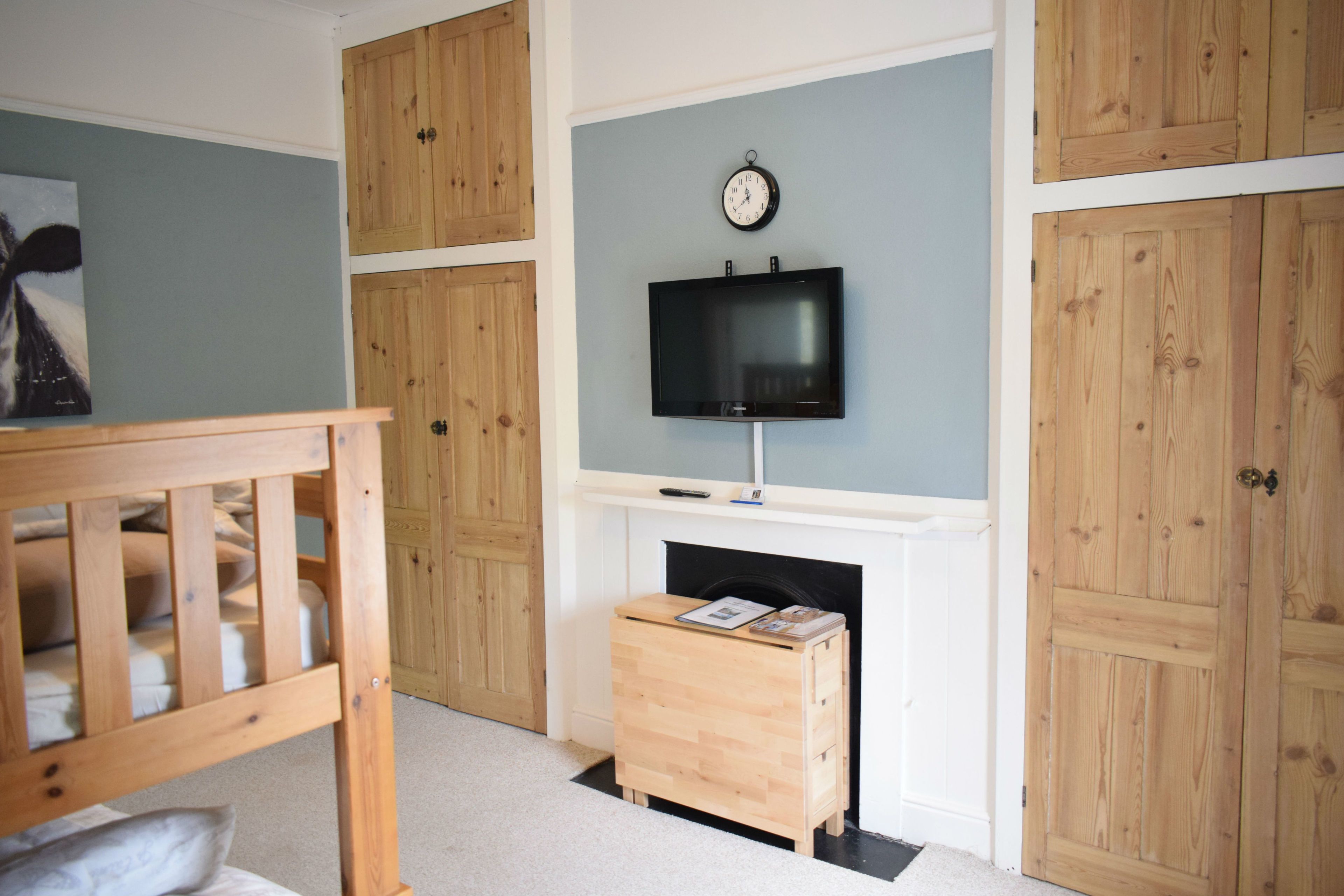 A room with a wooden crib, a fireplace, a television mounted above it, and wooden paneling on the walls.