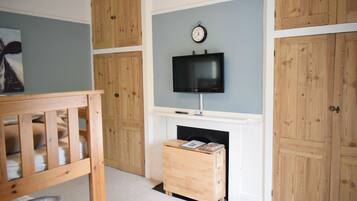 A room with a wooden crib, a fireplace, a television mounted above it, and wooden paneling on the walls.