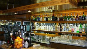 A bar area with shelves of liquor bottles, a fruit bowl, and glasses on the counter. - Hotel Serena (Grado)