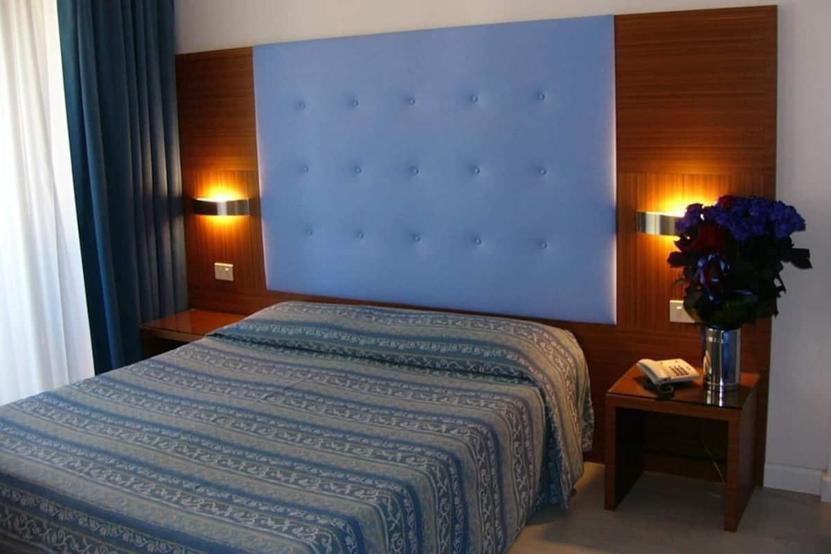 Une chambre d’hôtel avec un grand lit, une tête de lit en bois, deux lampes de chevet, une table de chevet avec un téléphone et un vase rempli de fleurs.