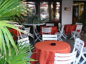Un área de estar al aire libre con mesas redondas cubiertas con manteles rojos y sillas blancas.
