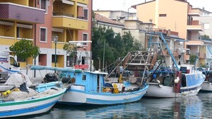 A row of boats docked at a marina with buildings in the background. - Hotel Serena (Grado)