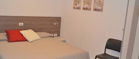 Un dormitorio con una cama, almohadas, una mesita de noche, una silla y tres cuadros en la pared.