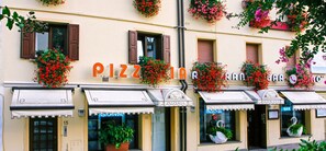 A row of pizzeria and bar establishments with awnings and flower baskets. - Hotel Cigno (Latisana)