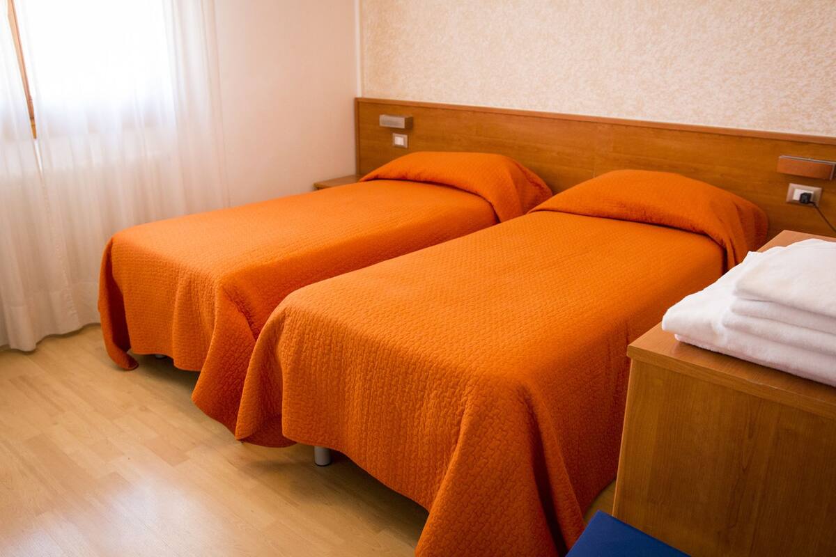 A hotel room with two single beds, wooden headboards, a wooden nightstand with a white towel, and a wooden floor.