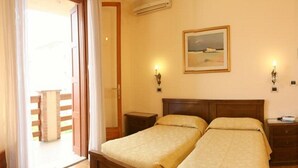 Habitación de hotel con dos camas, cabecera de madera, un cuadro en la pared y un balcón con baranda de madera.