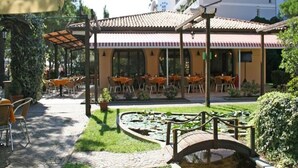 Un patio al aire libre con mesas y sillas, un pequeño estanque con nenúfares y una zona de estar cubierta con techo de baldosas.