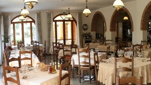 Un comedor con varias mesas dispuestas para comidas, sillas de madera y lámparas colgantes.