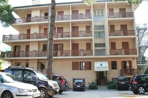 A multi-story hotel with balconies, a sign reading "Caffare di Orto," and several parked cars in front. - Capanna d'Oro (Lignano Sabbiadoro)