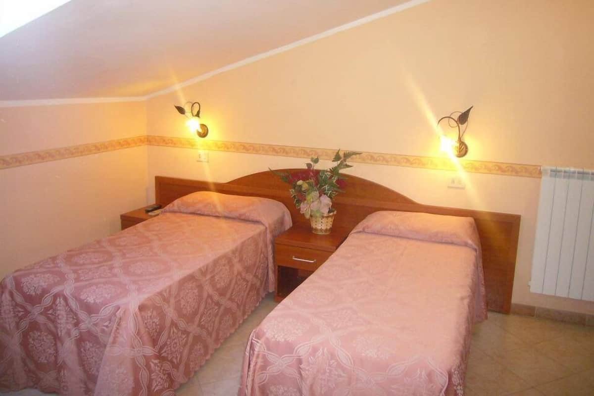 A room with two single beds, each with a floral-patterned bedspread, a bedside table with a vase of flowers, and wall-mounted lamps.