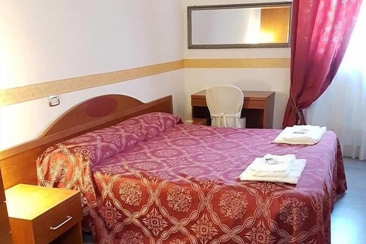 A hotel room with a bed, a desk, a chair, and a mirror on the wall.