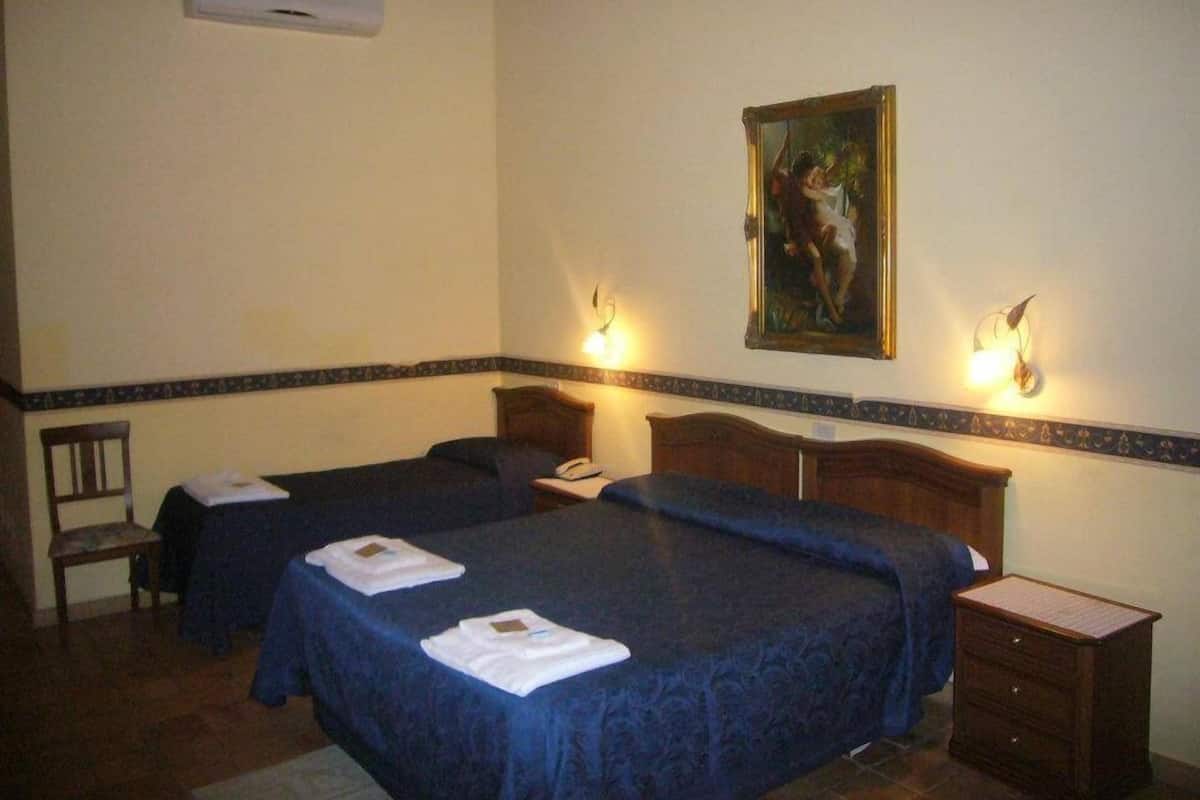 A hotel room with two single beds, a wooden nightstand, a chair, and a painting on the wall.
