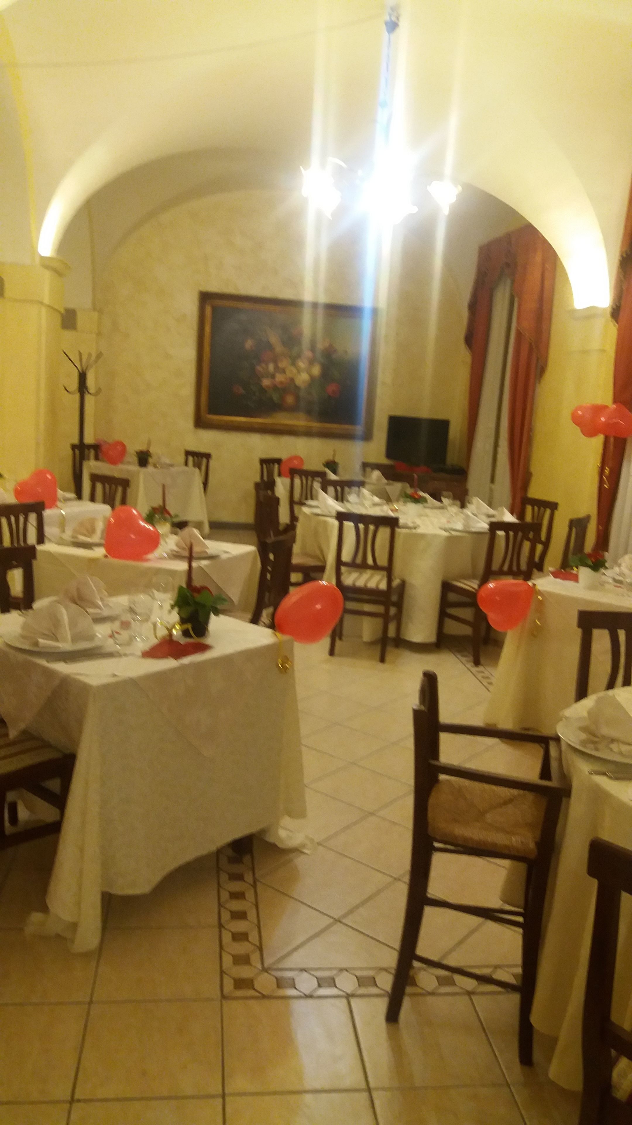 A dining area with tables set for a meal, featuring a tiled floor and a painting on the wall.