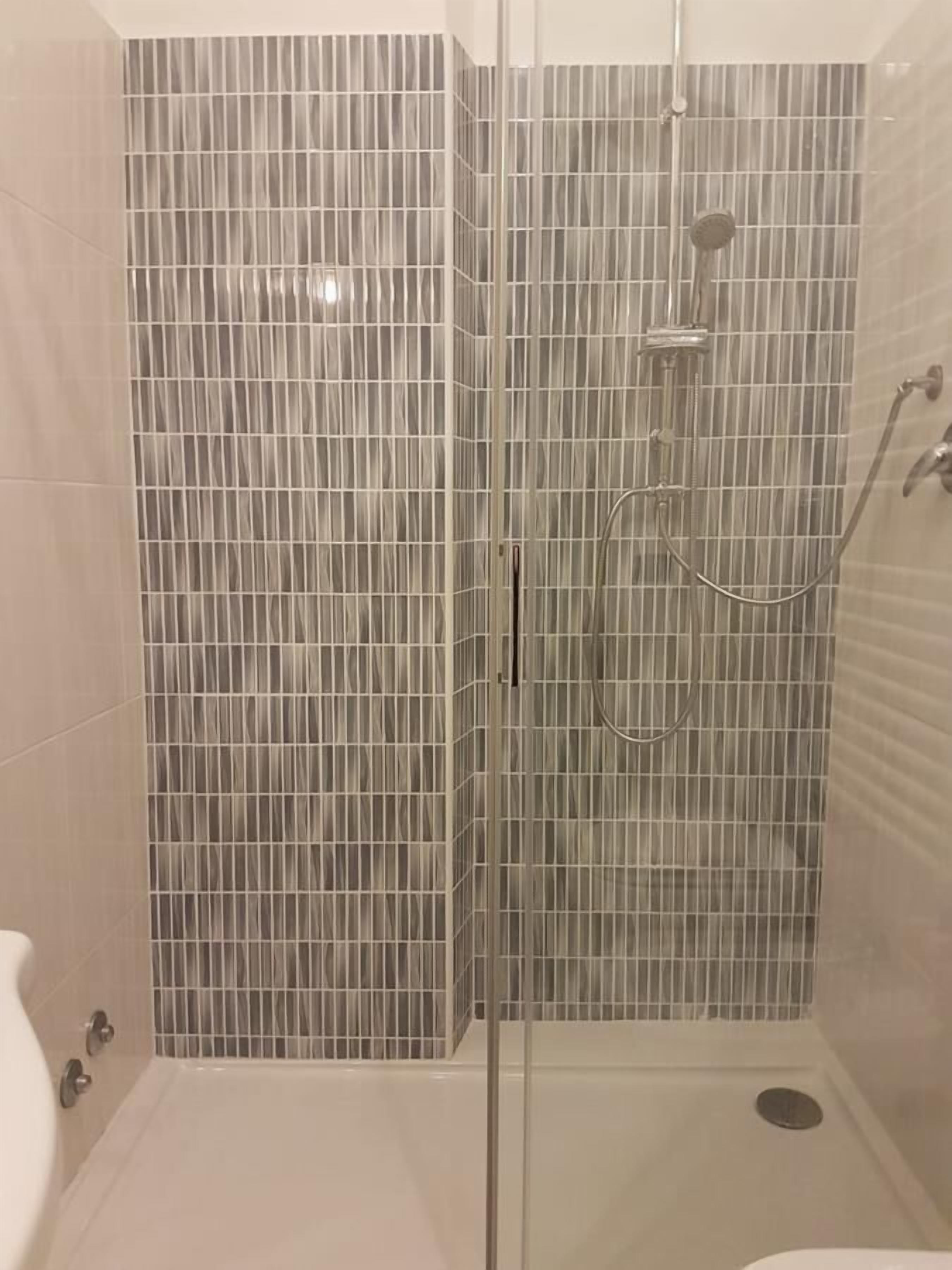 Eine Dusche mit Glastür und gefliesten Wänden.