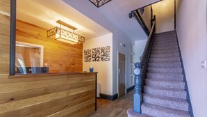 A reception area with a wooden reception desk, a patterned carpeted staircase, and a wall-mounted light fixture. - Woodcote Hotel (Ellesmere Port)