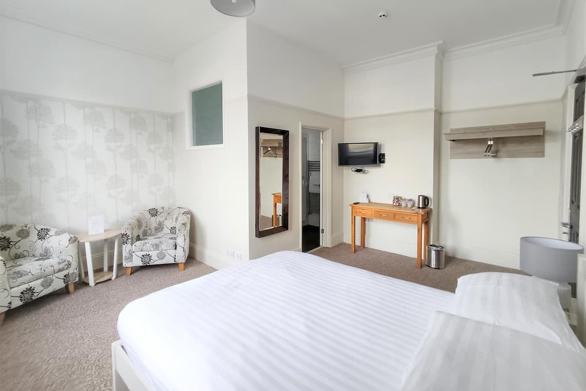 A hotel room with a large bed, a small desk, a chair, a television, and a mirror.