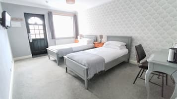 Une chambre d’hôtel avec deux lits simples, un bureau avec une chaise, une fenêtre avec des rideaux et un papier peint à motifs.