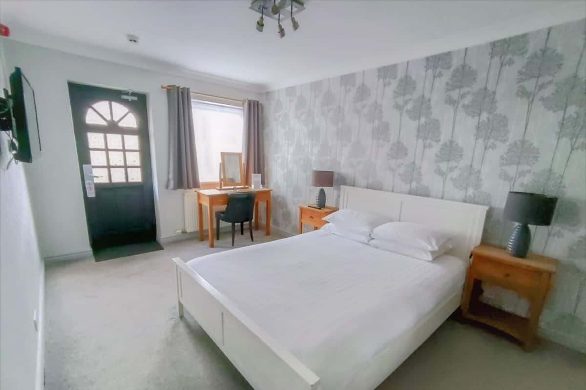 A bedroom with a large bed, a desk, a chair, a nightstand, and a door.