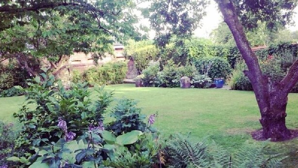 A well-maintained garden with a variety of plants and trees, a grassy lawn, and a stone wall in the background. - Woodcote Hotel (Ellesmere Port)