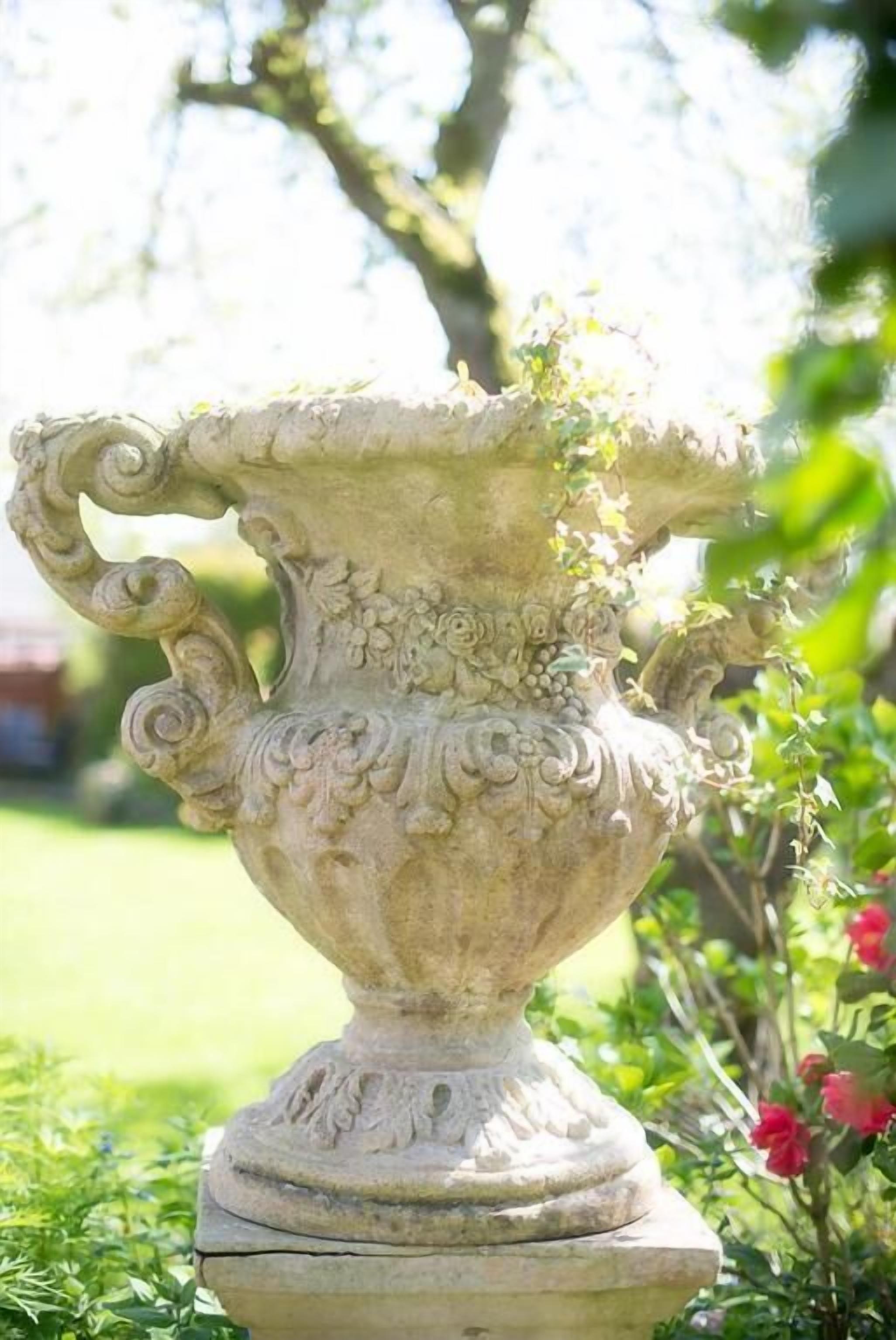 Um espelho de pedra com esculturas detalhadas, situado num jardim com vegetação e flores.