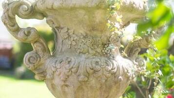 Um espelho de pedra com esculturas detalhadas, situado num jardim com vegetação e flores.