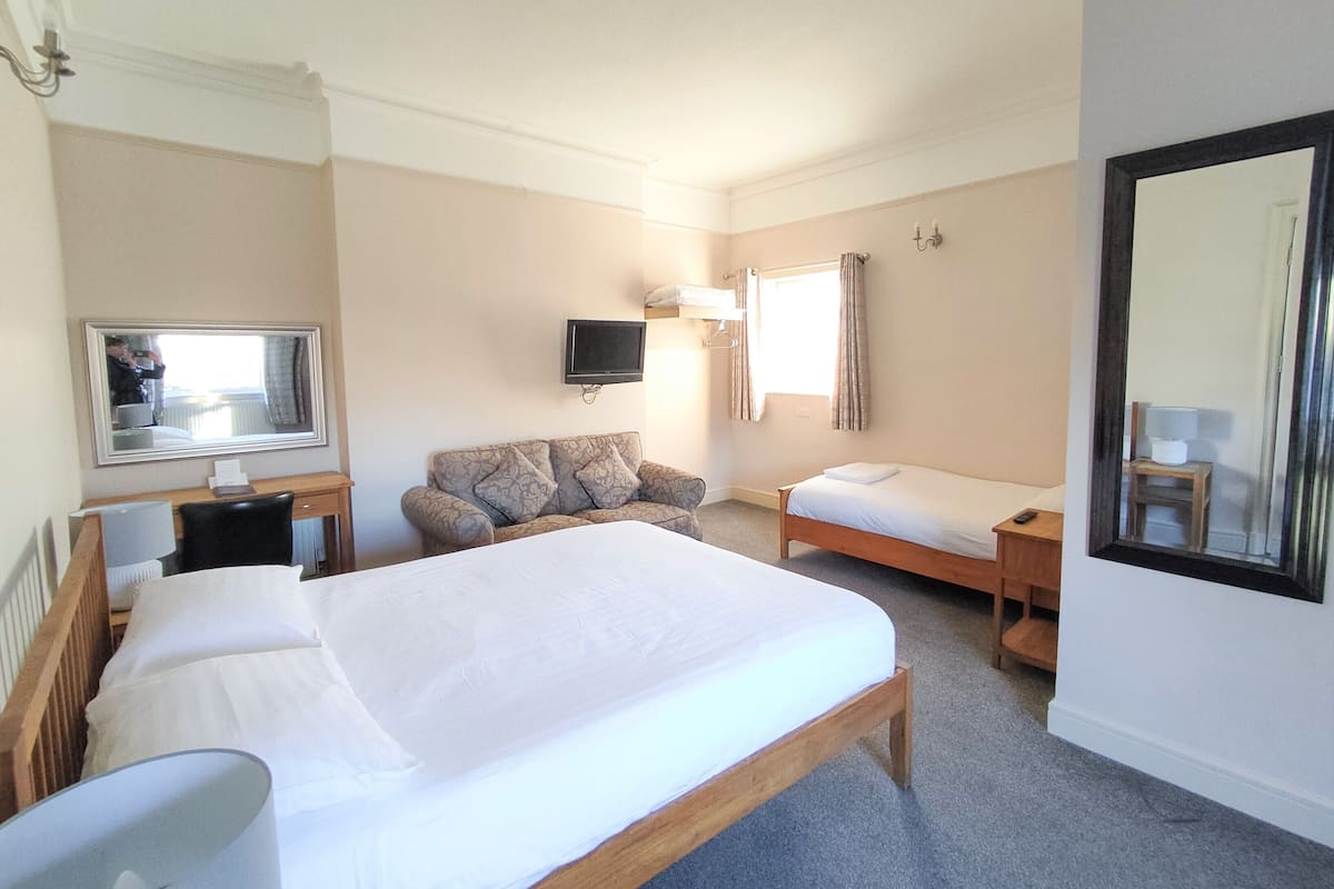 A hotel room with a large bed, a sofa, a desk, and a TV.