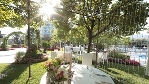 An outdoor dining area with round tables, white chairs, and a decorative centerpiece. - Edra Palace (Cassino)
