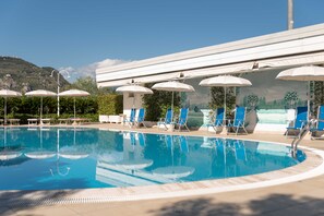 A swimming pool with lounge chairs and umbrellas, surrounded by a white building and greenery. - Edra Palace (Cassino)