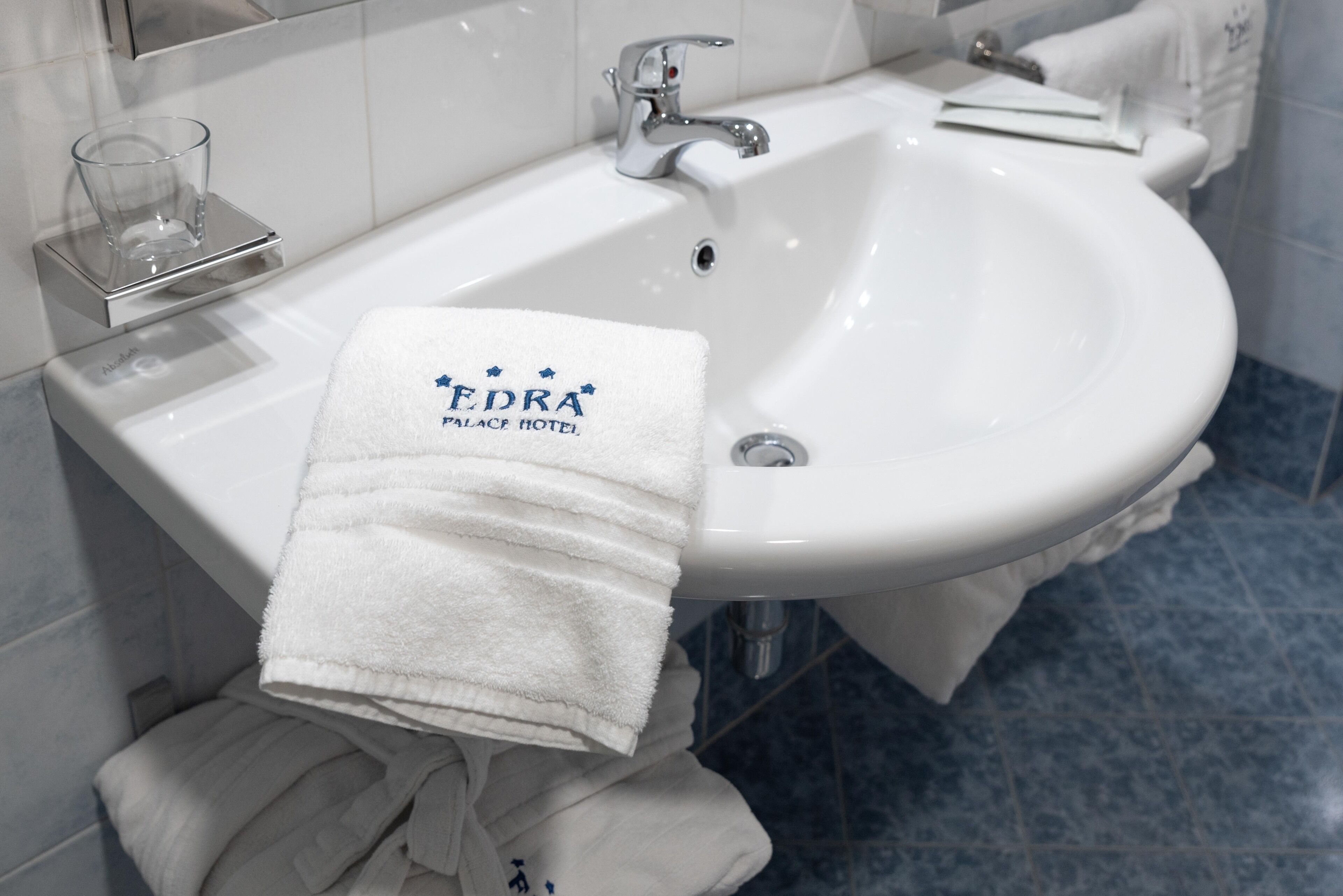 A white bathroom sink with a towel hanging on it, a glass on a soap dish, and a towel rack.