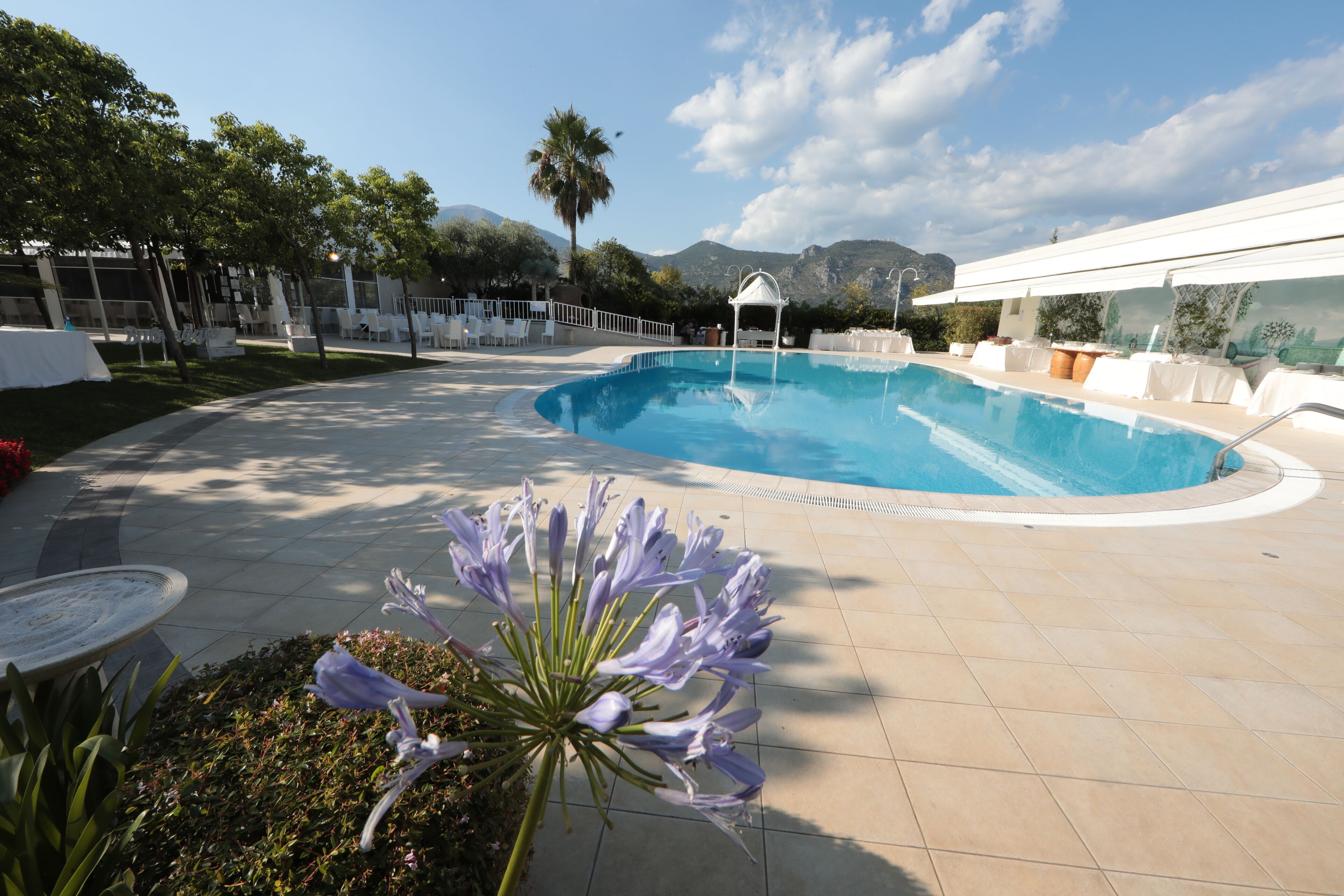 Une piscine agrémentée d’un belvédère, entourée de parasols blancs et de chaises, avec des montagnes en toile de fond.