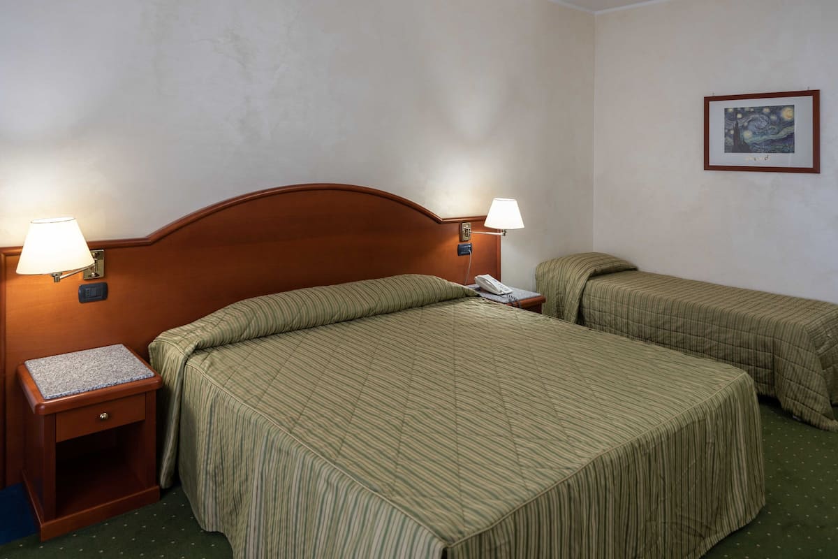 A hotel room with two single beds, each with a wooden headboard, a nightstand with a lamp, and a telephone.